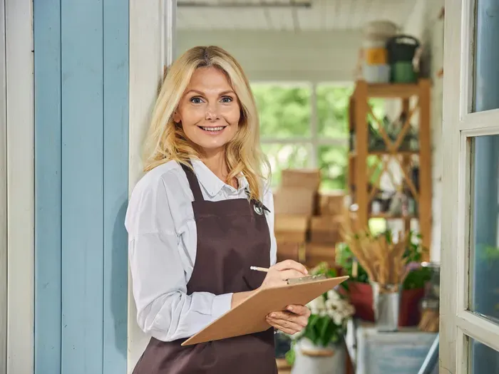 Female business owner standing at shop entrance with clipboard, smiling for towndirectoryportal.com